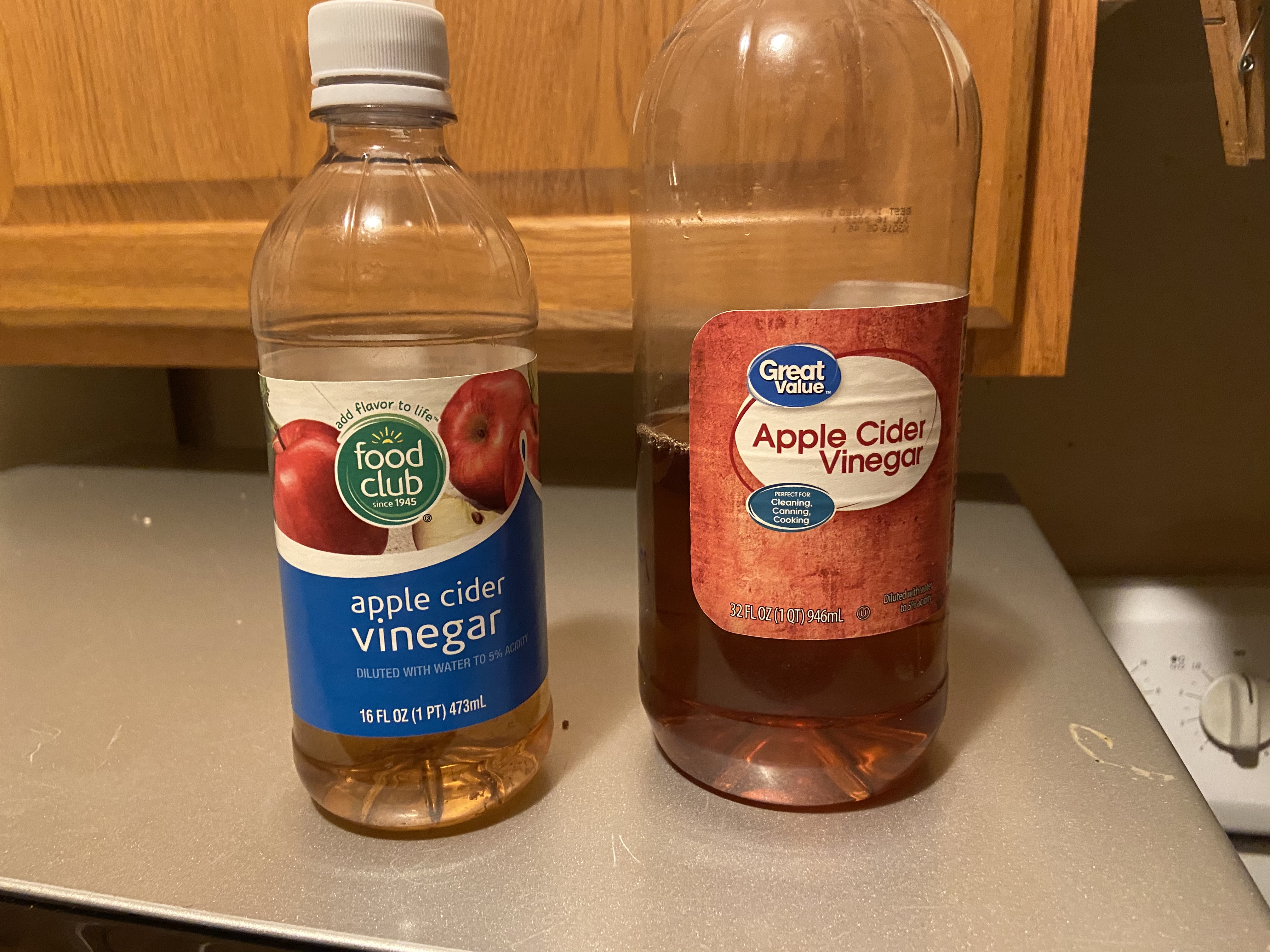Two bottles of Apple Cidar Vinegar. Both are roughtly 1/2 full. One is slightly larger than the other.